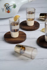 INVOKE Cabo White Rum with Coconut Liqueur in shot glasses with lemon garnish on wooden coasters.