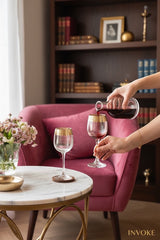 INVOKE elegant clear glass wine glasses with gold rim detail, one being filled with red wine.