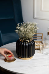 INVOKE Home and Living Vivid Vase: Matte black ceramic ribbed vase with gold rim and detailing, holding baby's breath flowers.