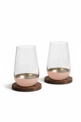 INVOKE Lusora high ball glass with clear tapered body, gold interior, and matte blush pink base on wood coasters.