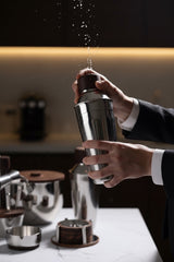 INVOKE Stainless Steel Barware Set with wooden accents, cocktail shaker in use.