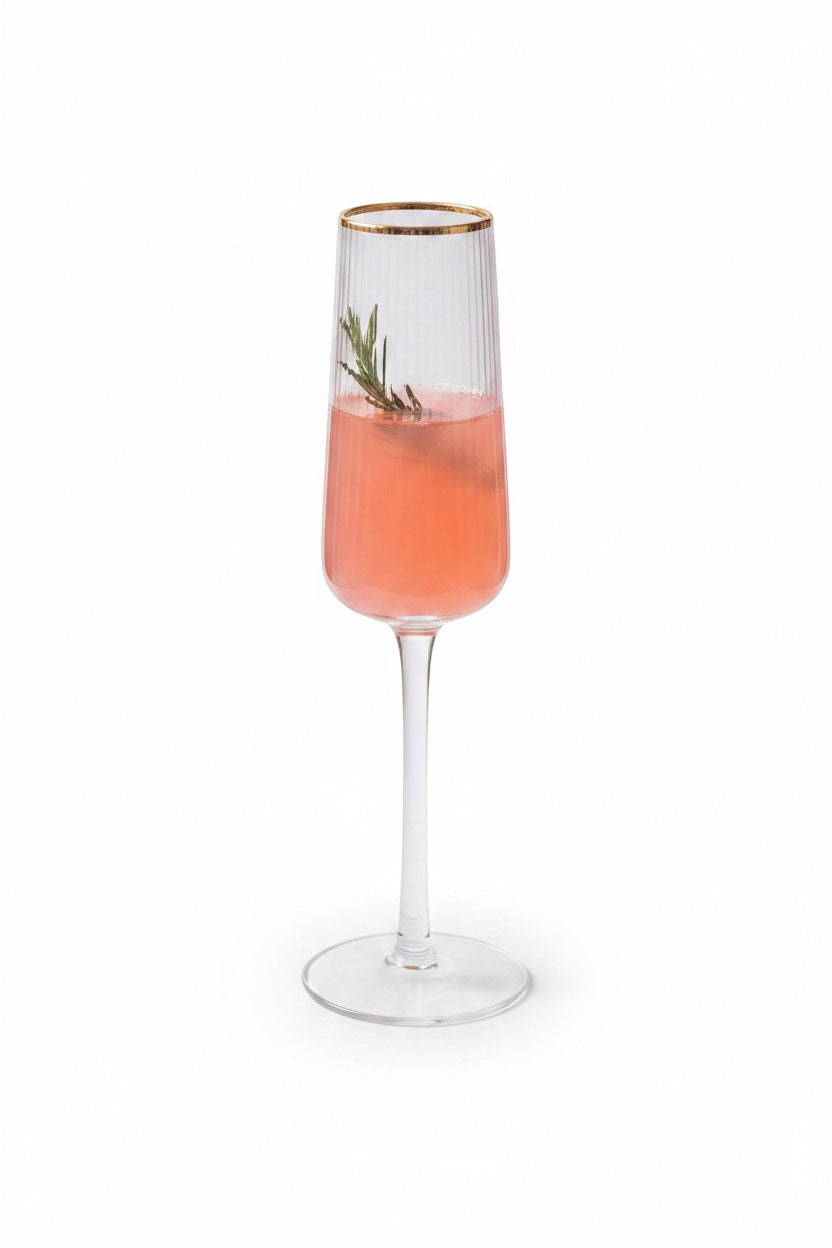 INVOKE fluted champagne flute with gold rim, ribbed glass, filled with pink champagne and a sprig of rosemary.
