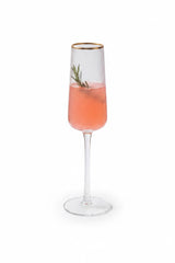INVOKE fluted champagne flute with gold rim, ribbed glass, filled with pink champagne and a sprig of rosemary.