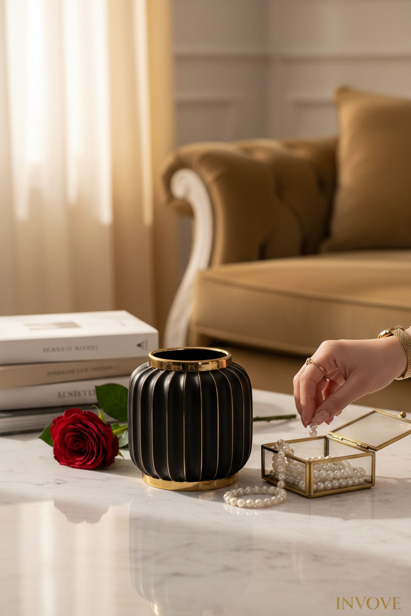 INVOKE Home and Living matte black ribbed ceramic vase with gold rim and base, featuring a red rose and pearl jewelry.
