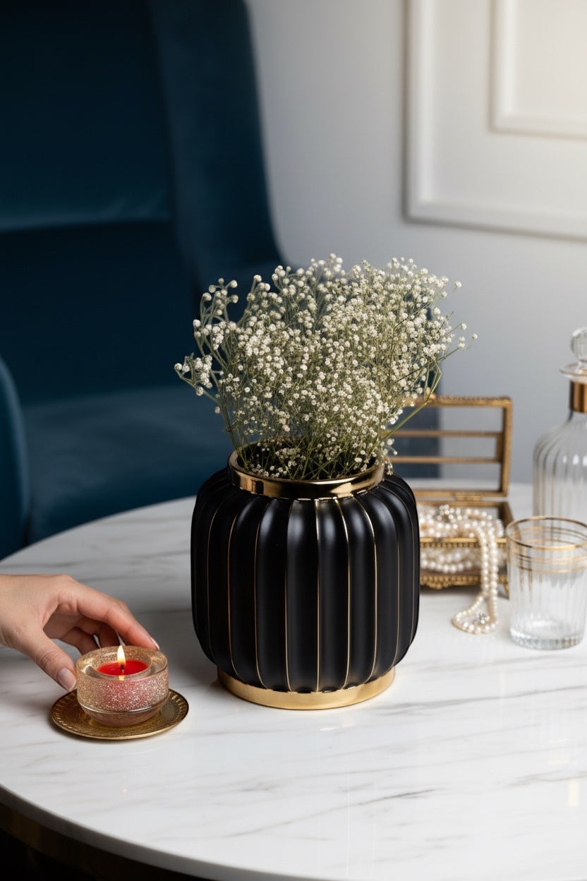 INVOKE Home and Living Vivid Vase: Matte black ceramic ribbed vase with gold rim and detailing, holding baby's breath flowers.