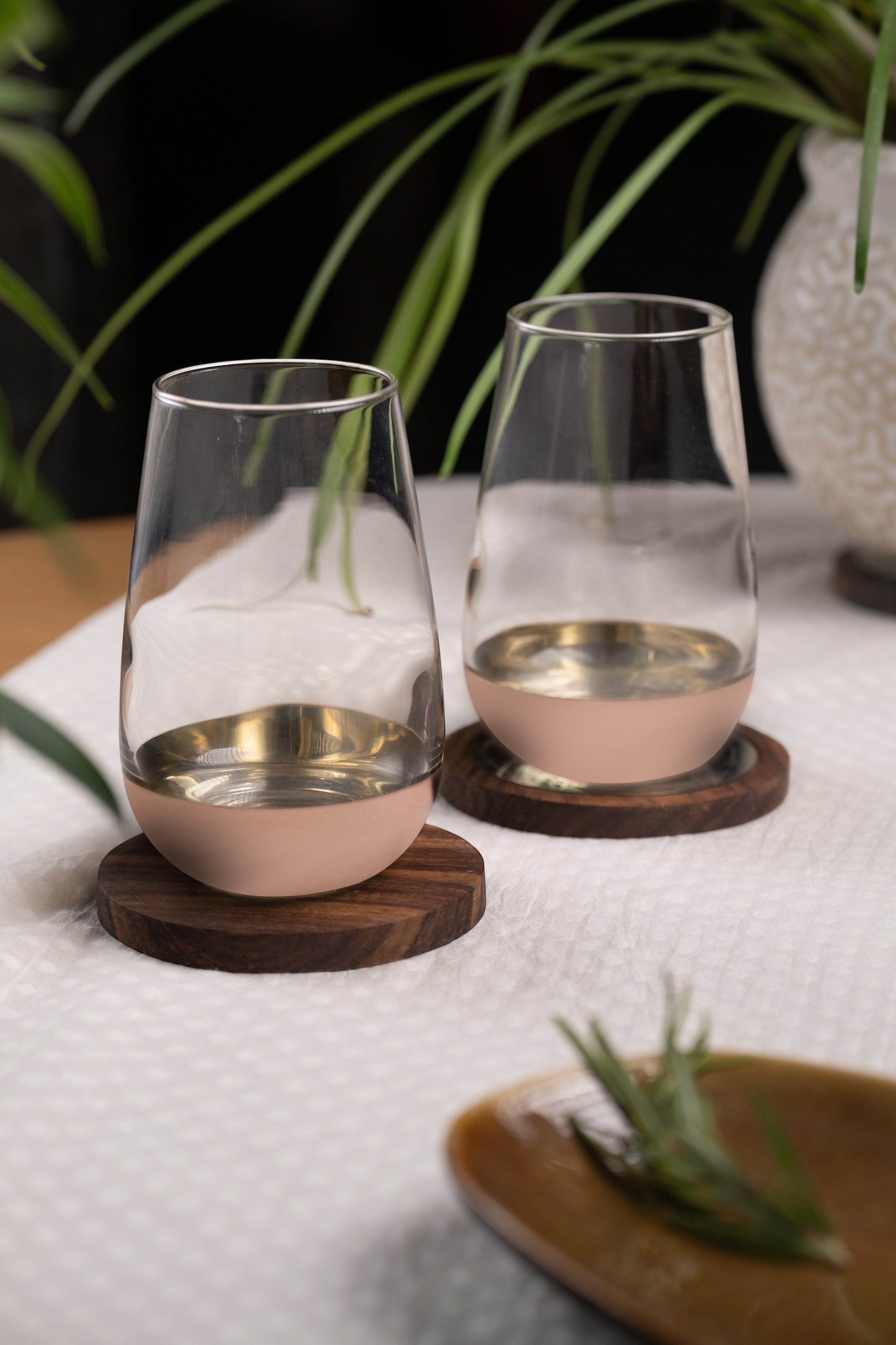 INVOKE Lusora High Ball Glass with gold interior and matte blush pink exterior base on wooden coasters.