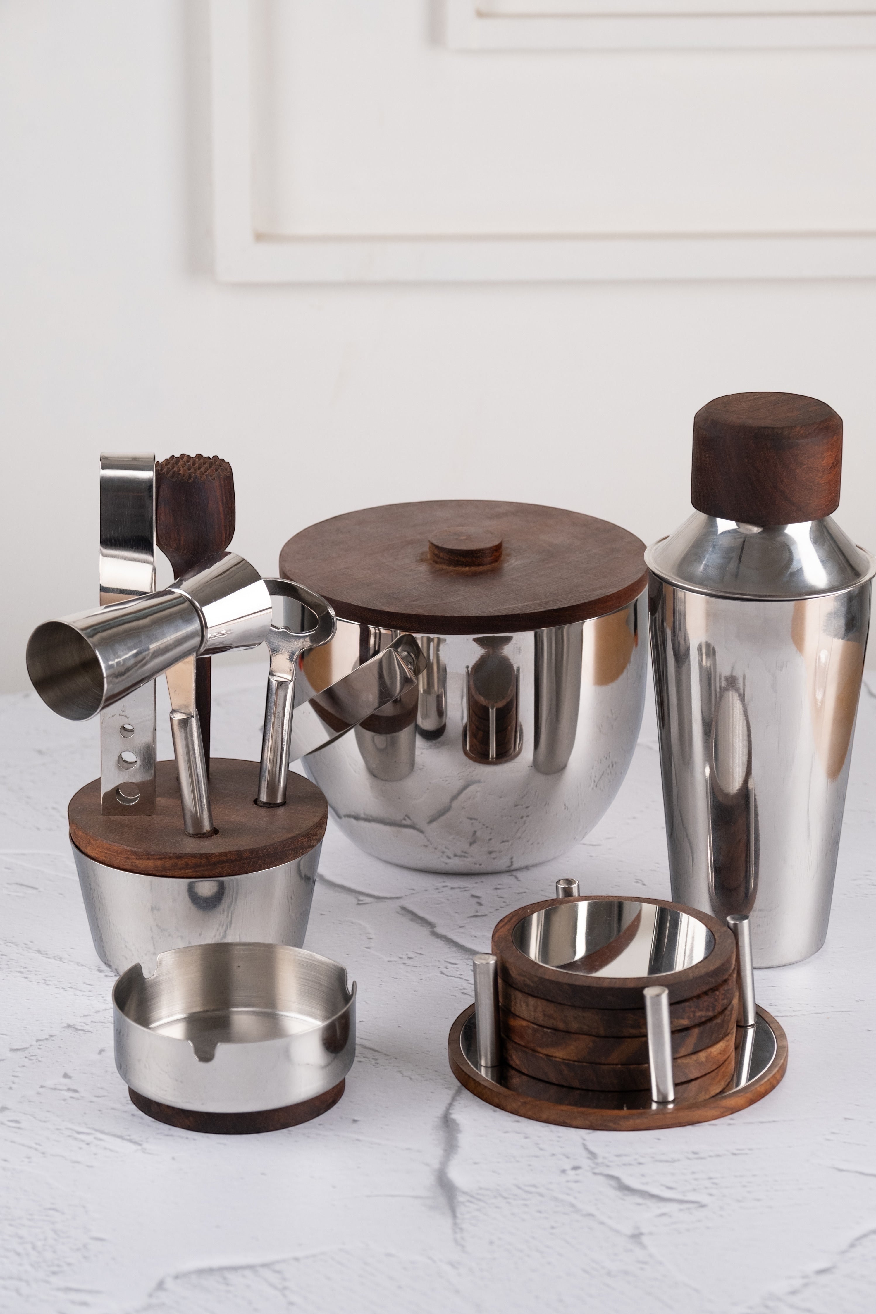 INVOKE Stainless Steel Barware Set with wooden accents, including shaker, ice bucket, jigger, coasters, and ashtray.